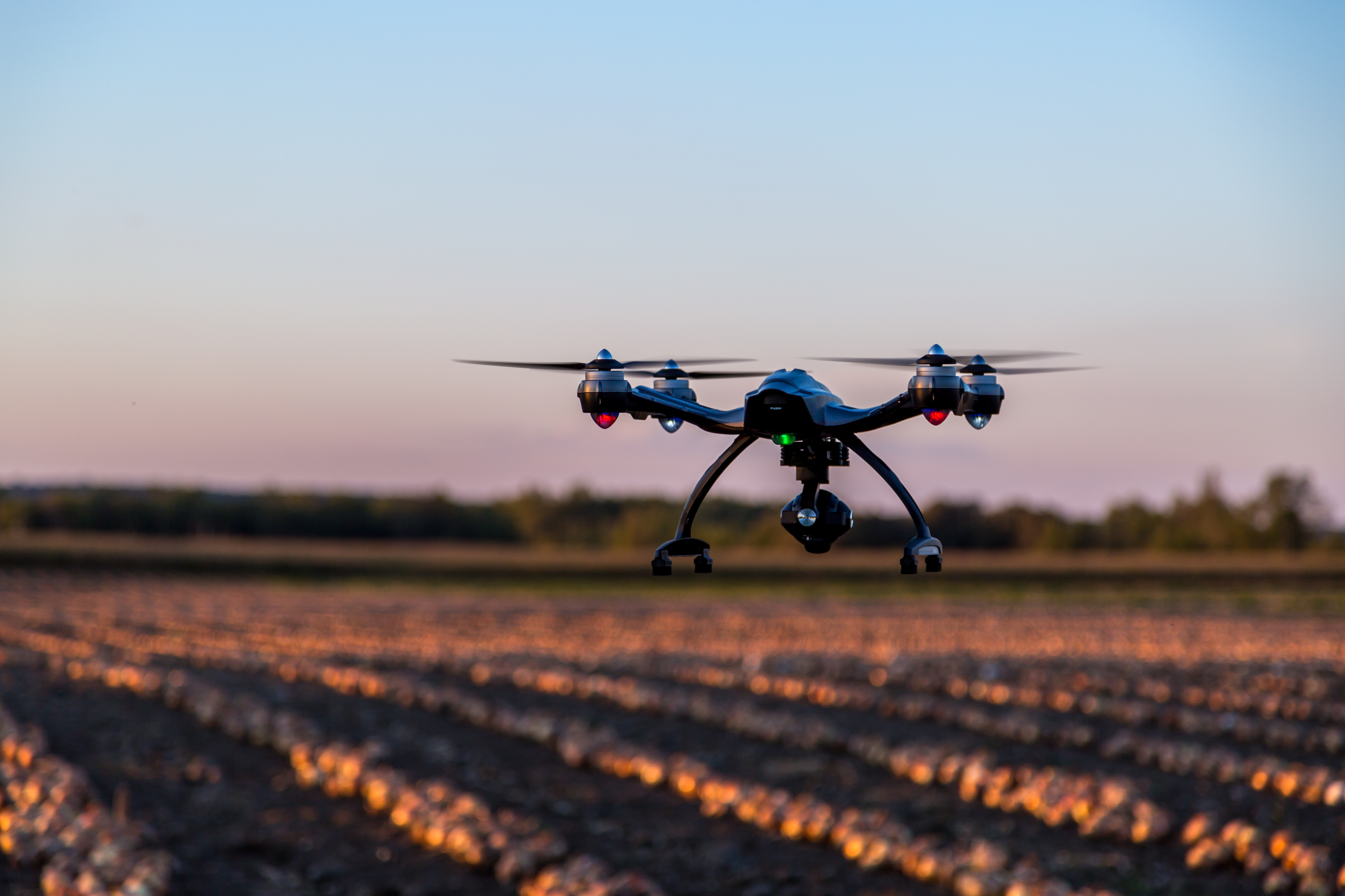 Drone with mounted camera is hovering over crops.